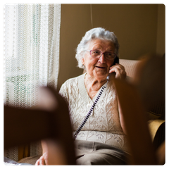 An older woman smiling while talking to someone on a landline telephone